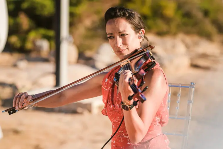 Violinist in a coral dress playing during the beach ceremony at Codolar, Salinas