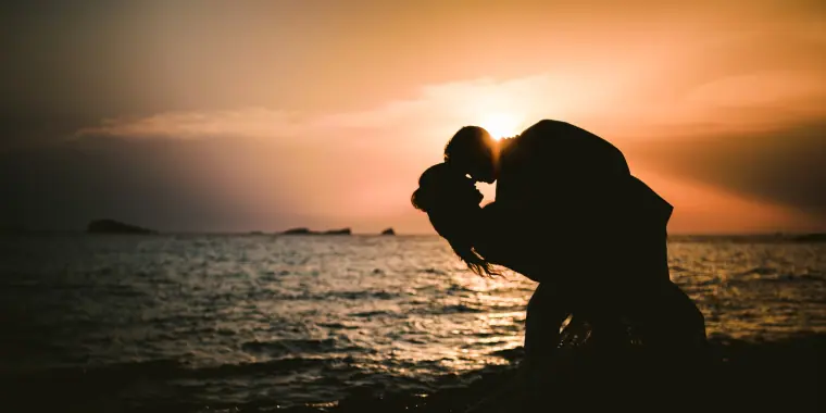 Kenton and Hassiba silhouetted in a kiss against a hazy sunset over the sea, Ibiza