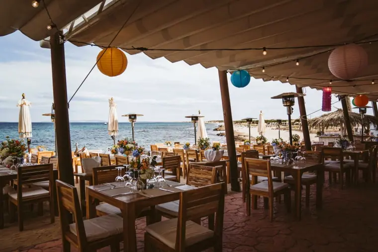 Beachfront restaurant terrace with paper lanterns and laid tables at Restaurante La Escollera, Ibiza