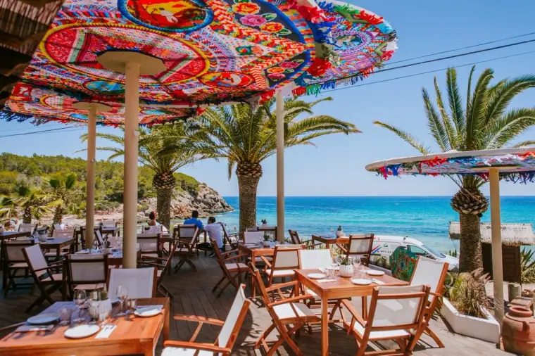 Beach restaurant with colourful patterned parasols and palm trees overlooking the sea, Ibiza