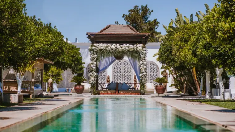 Long pool flanked by palms leading to a white flower-draped pavilion at an Ibiza venue