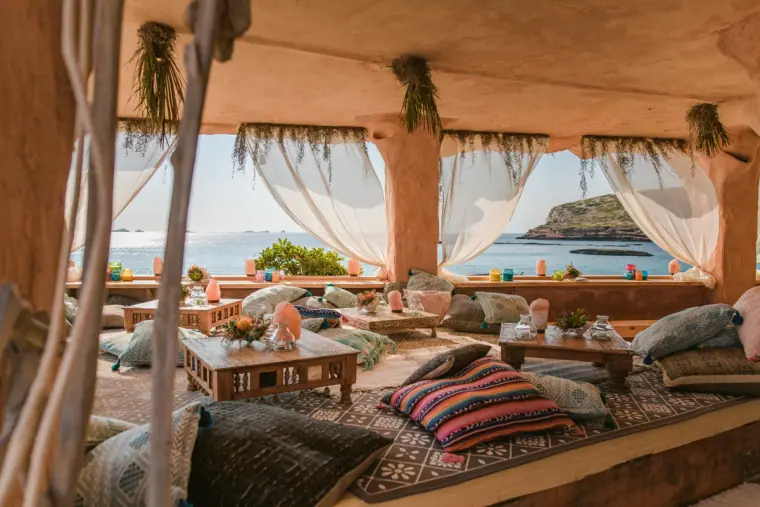 Shaded boho lounge with floor cushions and sea views through draped curtains, Sunset Ashram, Cala Conta