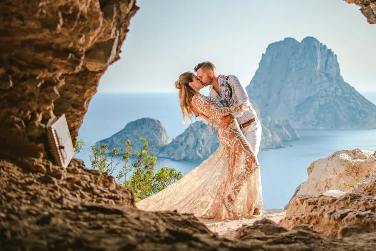 Kenton and Hassiba embracing within a rocky cave mouth facing Es Vedrà, Ibiza