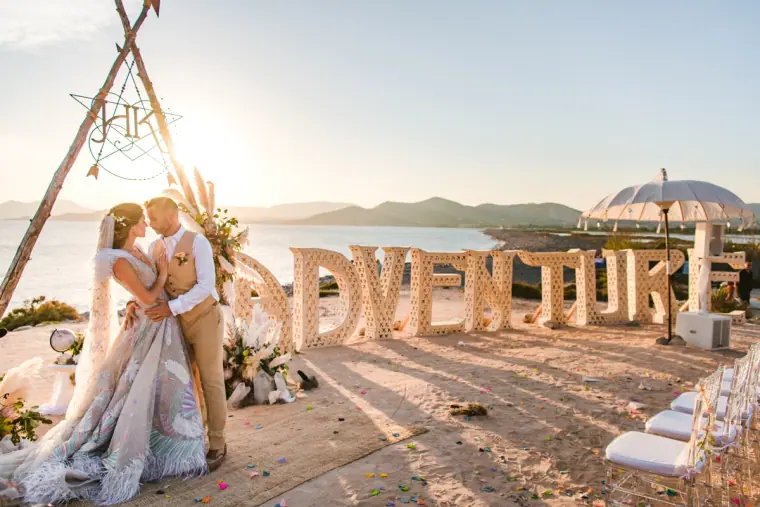 Kenton and Hassiba by a driftwood arch and giant ADVENTURE letters on the beach, Codolar, Salinas