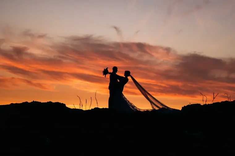 Silhouette of a bride and groom with a sweeping veil under a red sunset at Alassos