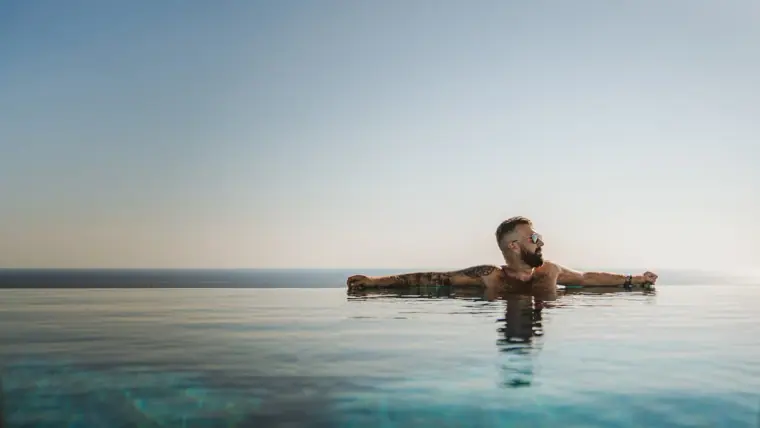 Man relaxing at the edge of the infinity pool at Napa Suites, looking out to sea