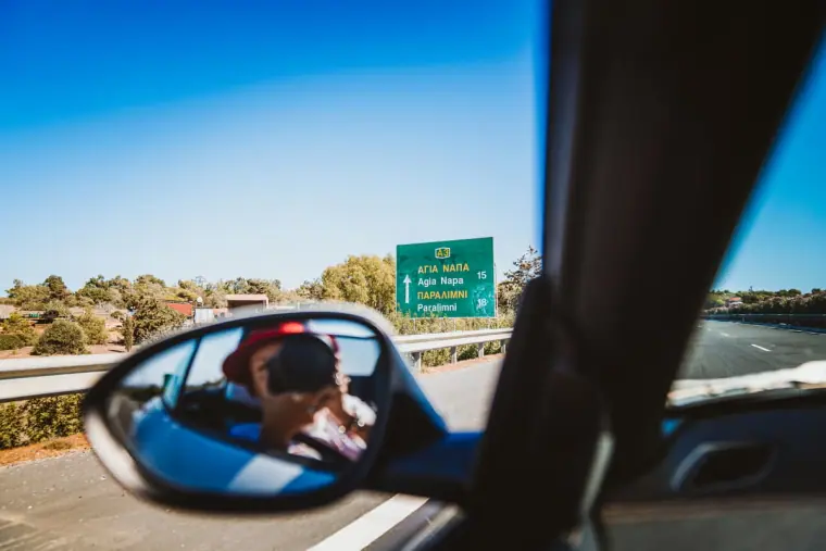 View through a car wing mirror of a road sign for Agia Napa on the drive in