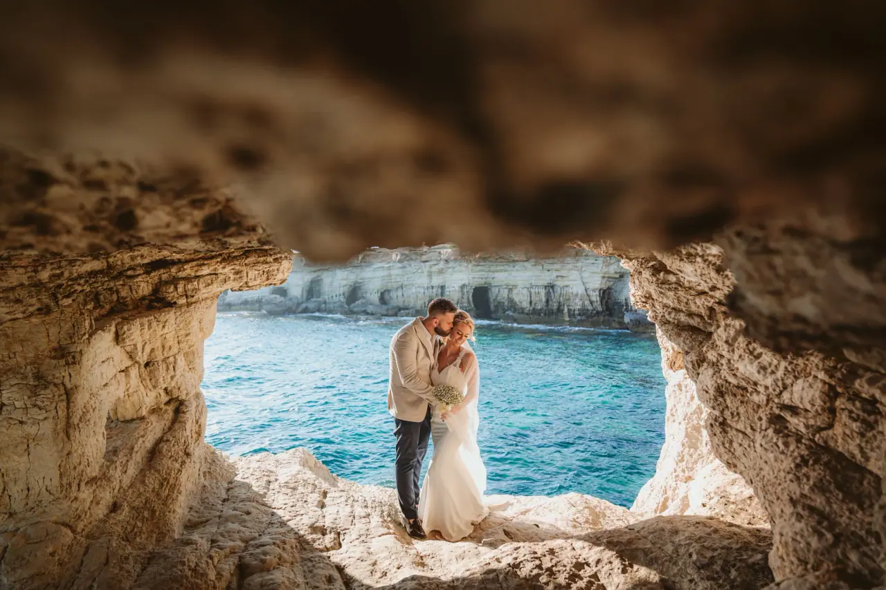 Adele and Nelly embracing in a rocky sea cave above turquoise water, Ayia Napa