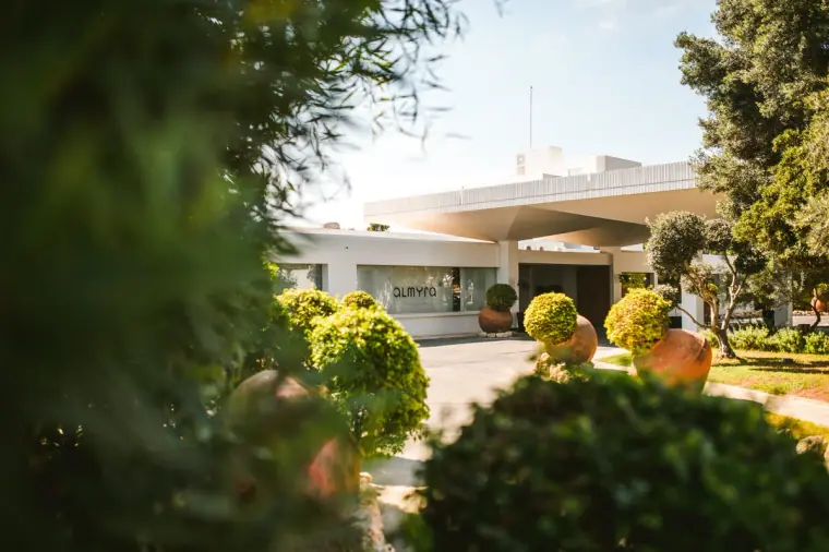 Almyra hotel entrance glimpsed through garden greenery on a sunny day, Paphos