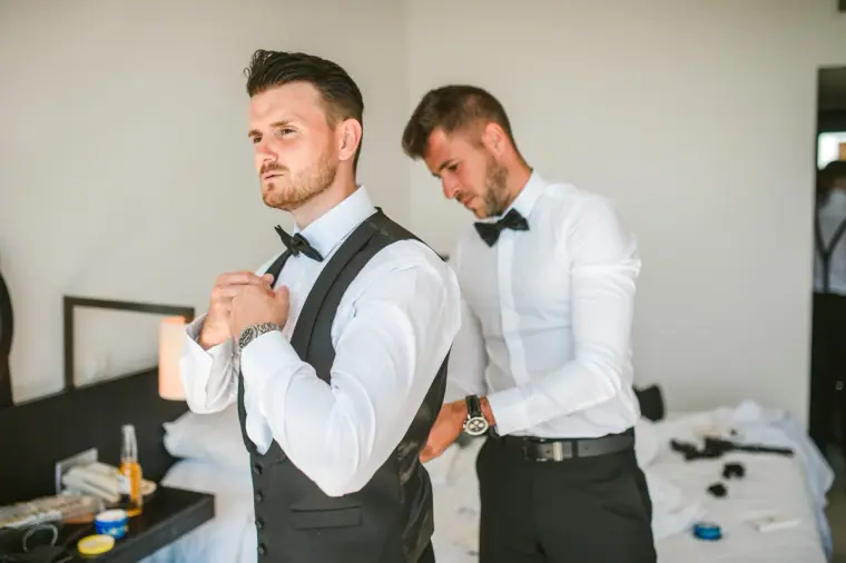 Groomsmen helping with bow ties and waistcoats while getting ready at Almyra
