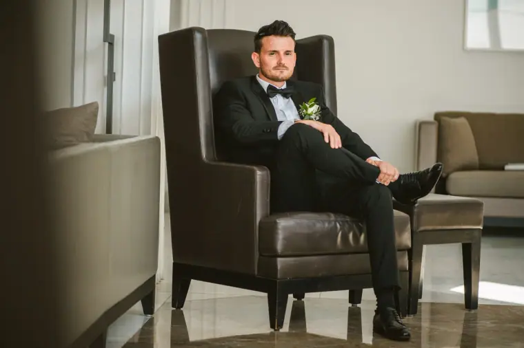 Steven relaxing in his tuxedo in a brown leather armchair at Almyra