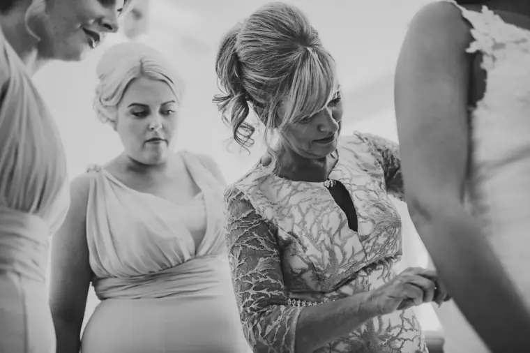 Black-and-white photo of bridesmaids and a woman in lace helping with final touches