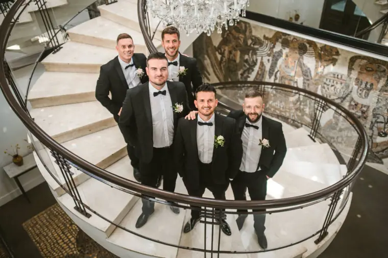 Steven and his groomsmen in tuxedos posing on a spiral staircase at Almyra