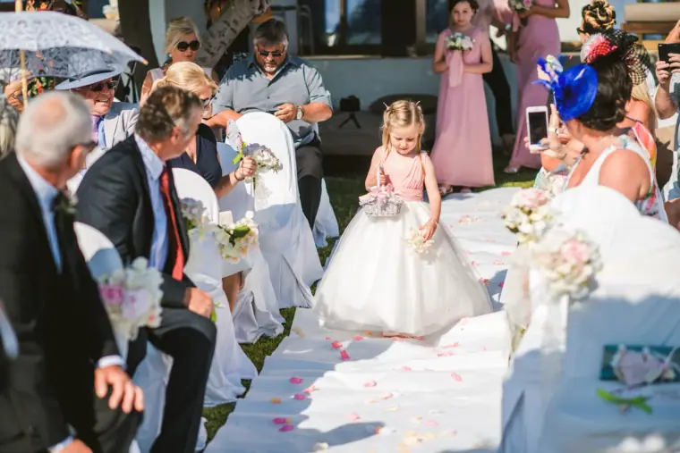 Flower girl in a white tutu dress walking down the aisle between guests