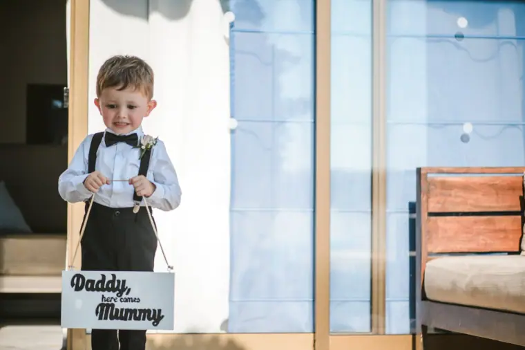 Page boy in braces holding a 'Daddy, here comes Mummy' sign