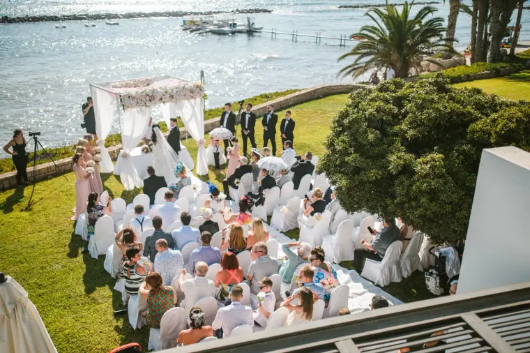 Elevated view of the seaside lawn ceremony with guests seated in white chairs, Almyra, Paphos