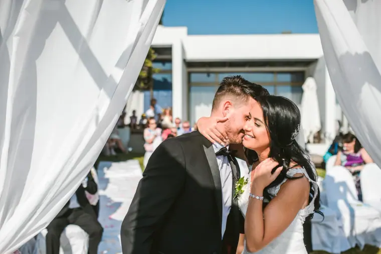 Jaclyn and Steven sharing their first kiss as husband and wife beneath white drapes
