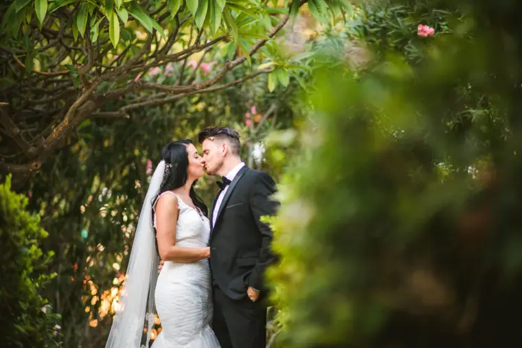 Jaclyn and Steven kissing among leafy greenery in the Almyra gardens