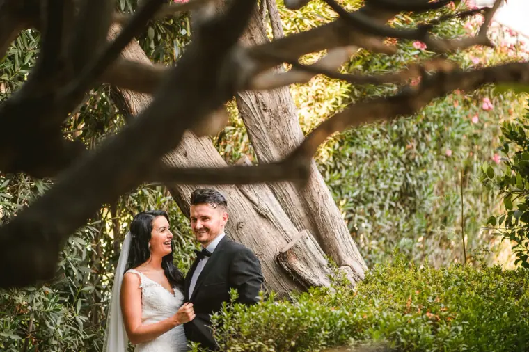 Jaclyn and Steven embracing beneath the twisting branches of an old tree in the Almyra gardens