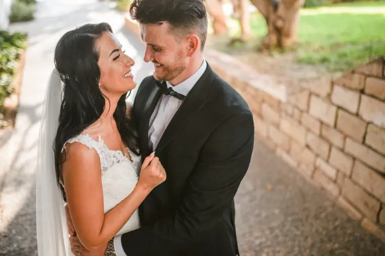 Jaclyn and Steven laughing together beside a stone wall in the Almyra gardens