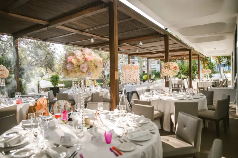 Reception tables with pink floral centrepieces under a shaded terrace at Almyra, Paphos