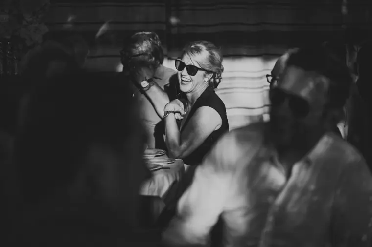 Black-and-white photo of a guest in sunglasses laughing and dancing at the reception