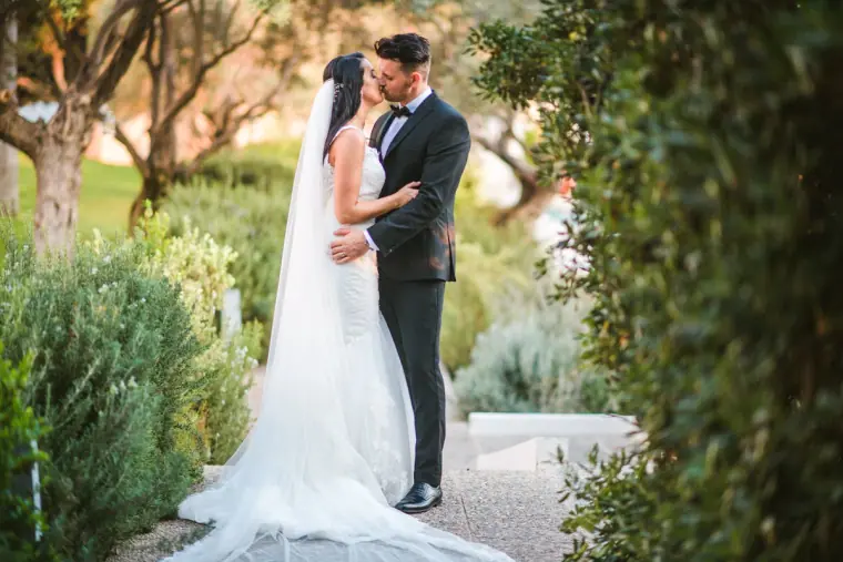 Jaclyn and Steven kissing on a garden path, her veil trailing on the ground