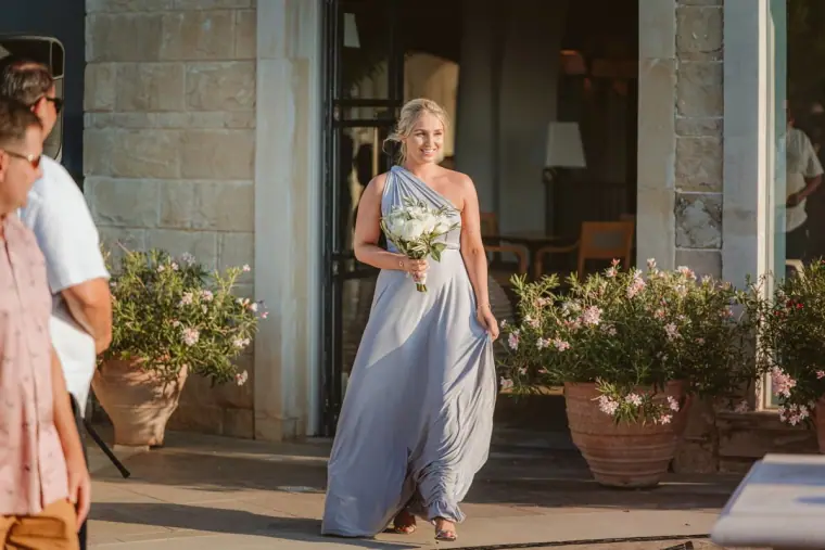 Bridesmaid in a lilac gown walking down the aisle with a white bouquet