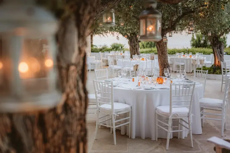Lantern on an olive tree beside white dinner tables set for the reception