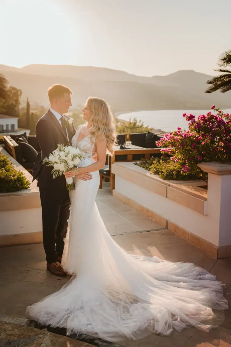 Bride and groom on the terrace with a long tulle train and sea view at sunset