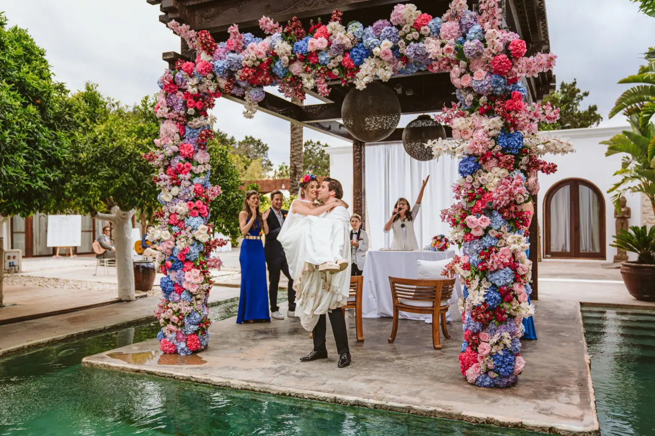 Antonia and Birger beneath a colourful floral arch on a pool platform at Atzaro, Ibiza
