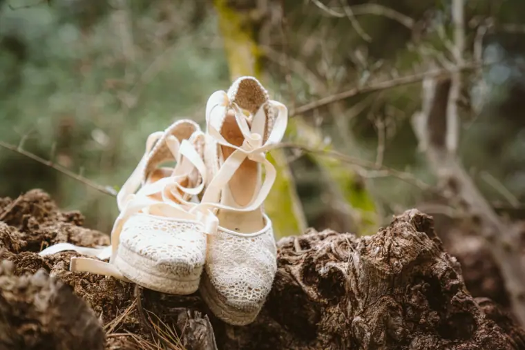 White lace espadrille wedding shoes resting on a rock