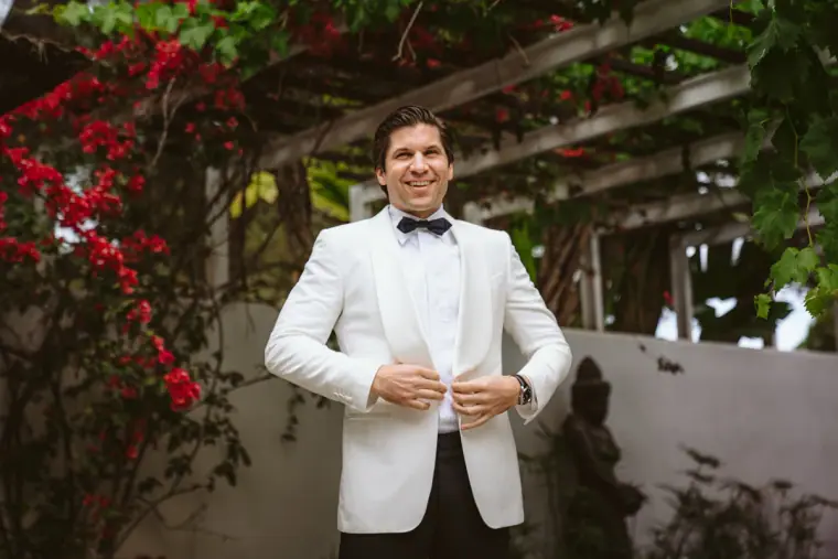 Birger buttoning his white dinner jacket beneath red bougainvillea at Atzaro