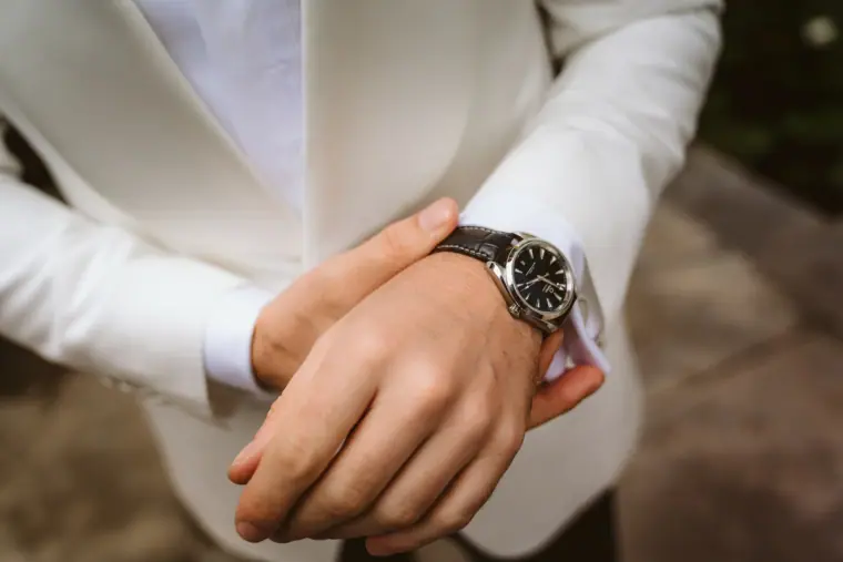 Close-up of the groom's hands and watch against his white tuxedo jacket