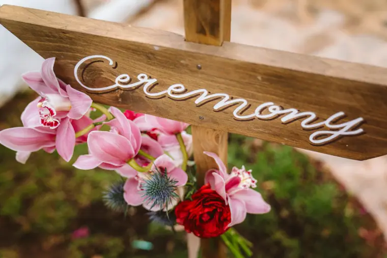 Wooden ceremony sign in white script decorated with pink orchids
