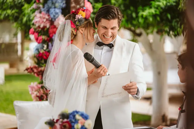 Bride reading her vows into a microphone as Birger laughs beside her at Atzaro