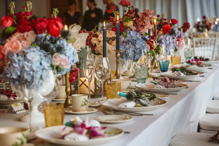 Long dinner table dressed with red roses, hydrangeas, candles and gold cutlery