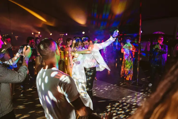 Groom in a white jacket dancing with guests under colourful party lights