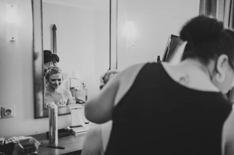 Black-and-white photo of the bride reflected in a mirror as her hair is styled