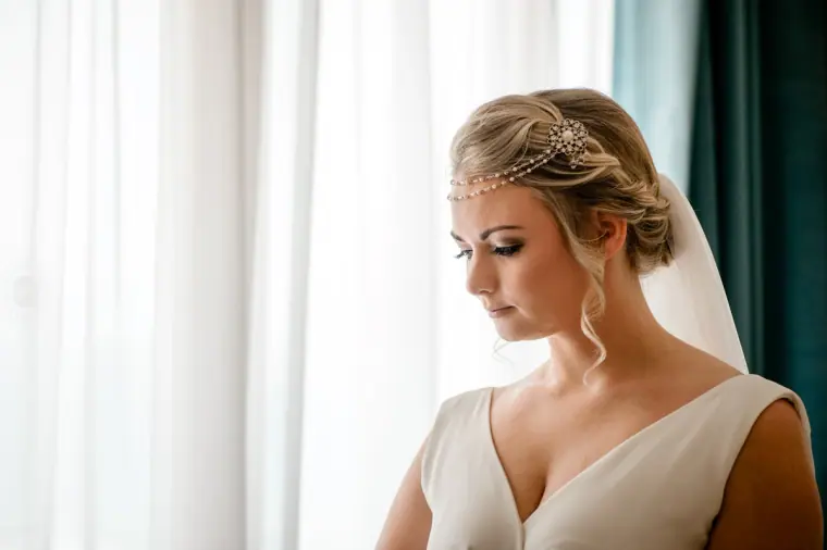 Close portrait of the bride in a jewelled hair vine looking down by a window