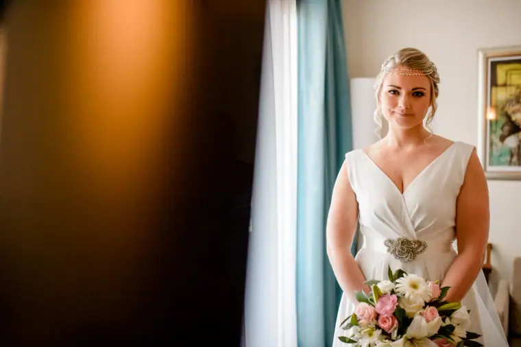 Francesca standing by the window holding a pink and white bouquet