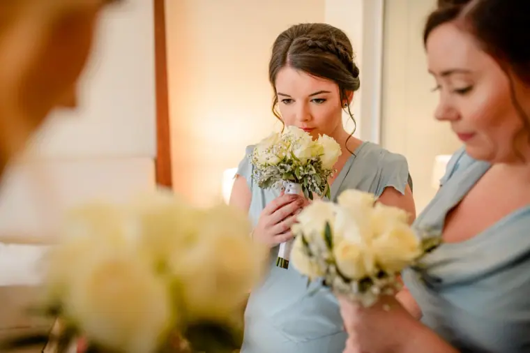 Bridesmaids in pale blue smelling their white rose bouquets