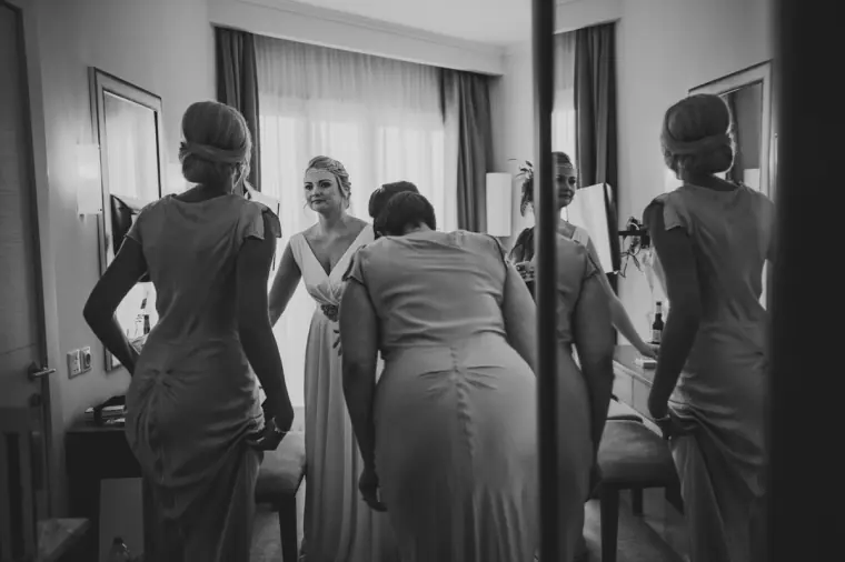 Black-and-white photo of the bride surrounded by bridesmaids making final adjustments