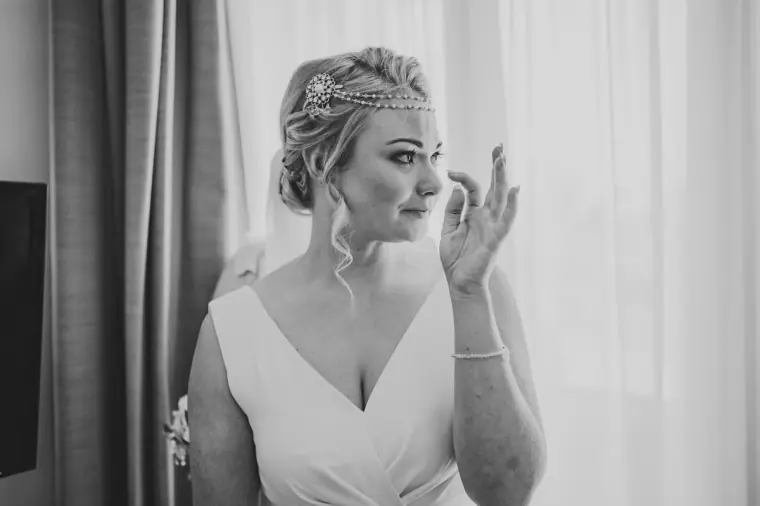 Black-and-white photo of the bride wiping away a tear by the window