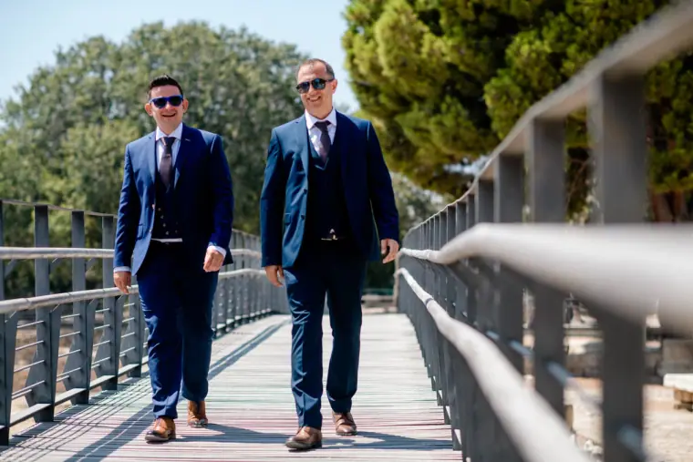 Stephen and a groomsman in navy suits walking along a wooden walkway, Paphos