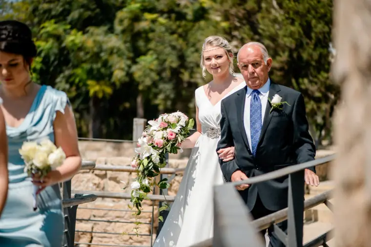Francesca on her father's arm walking past the ruins to the church, Paphos
