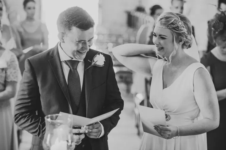 Black-and-white photo of the bride and groom smiling as they read their order of service