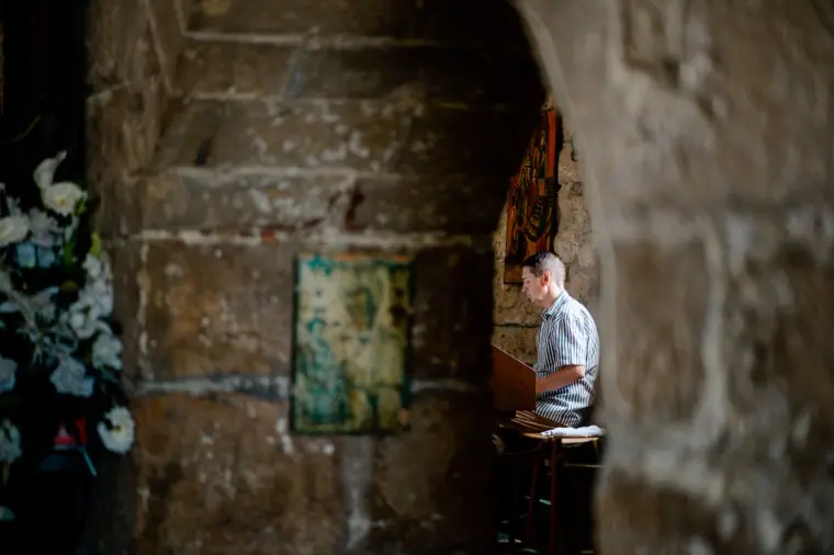 Glimpse through stone arches of a man at the front of the church during the service