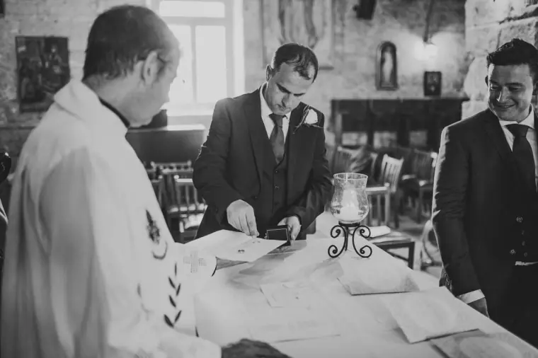 Black-and-white photo of the groom signing the register beside the priest