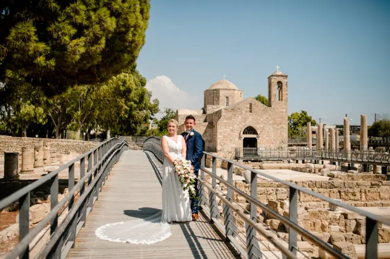 Couple on the wooden walkway with Ayia Kyriaki church and ruins behind, Paphos